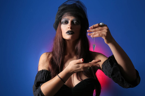 Malvagia giovane strega con pendolo su sfondo di colore - Foto, immagini