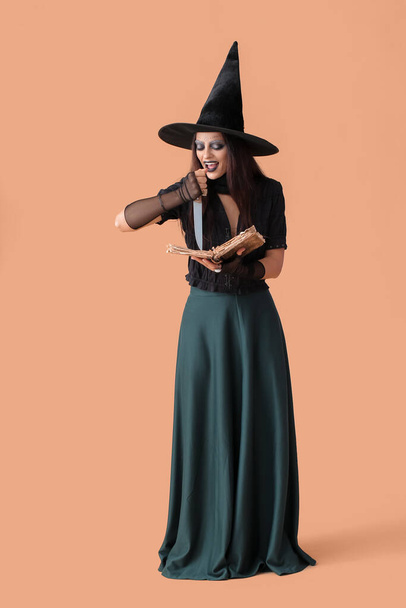 Unheimliche junge Hexe mit Zauberbuch und Messer auf farbigem Hintergrund - Foto, Bild
