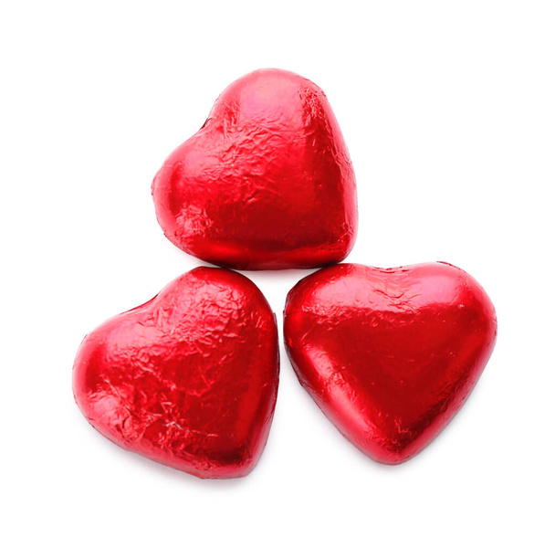 Dulces de chocolate en forma de corazón en papel de aluminio rojo sobre fondo blanco, vista superior - Foto, imagen