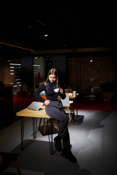 Normal working day of modern woman businessman. Beautiful young woman holding a cup of coffee while sitting at her workplace - Photo, Image