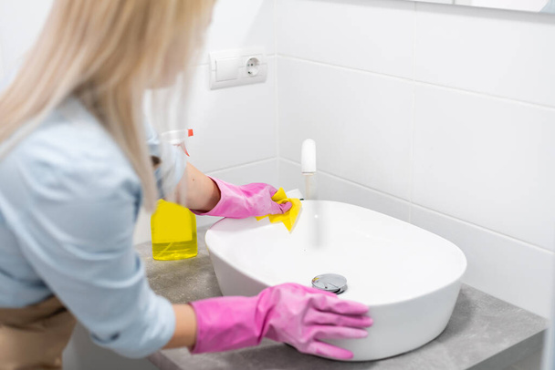 Domácí práce a domácí životní styl: žena dělá domácí práce v koupelně doma, mytí umyvadla a kohoutku s čisticím prostředkem - Fotografie, Obrázek
