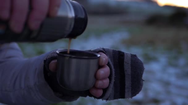 Mãos em mitenes derramando bebida de garrafa térmica no dia de inverno - Filmagem, Vídeo