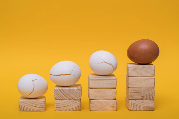Abstracción, metáfora, una escalera de carrera improvisada, un huevo de oro entero e irrompible yace y tres huevos blancos y estallidos yacen en el camino hacia la meta. - Foto, imagen