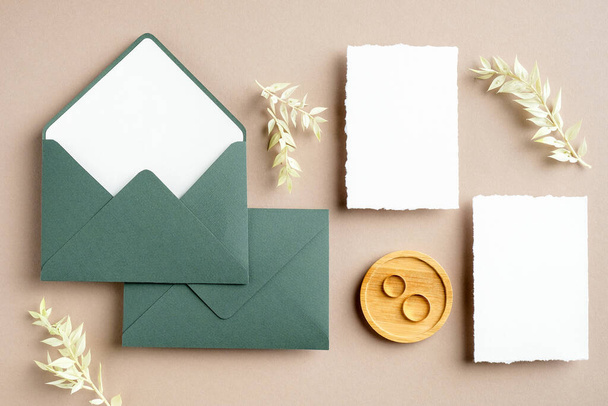 Feminine wedding stationery set. Blank greeting card, green envelopes, dried flowers, golden rings on pastel beige background. Rustic wedding invitation cards. Flat lay, top view, copy space. - Photo, image