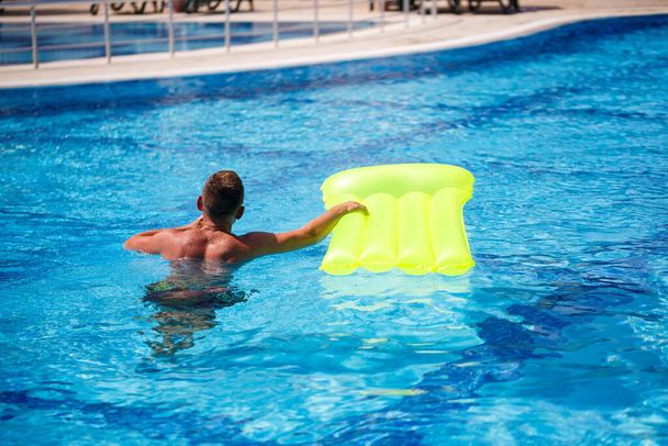 Handsome young man swims on inflatable mattress in blue pool - Photo, Image