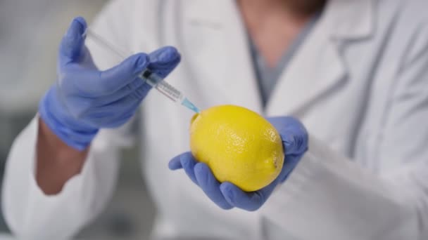 Primer plano de tecnólogo irreconocible inyectando vitamina C artificial al limón modificado genéticamente en el laboratorio - Metraje, vídeo