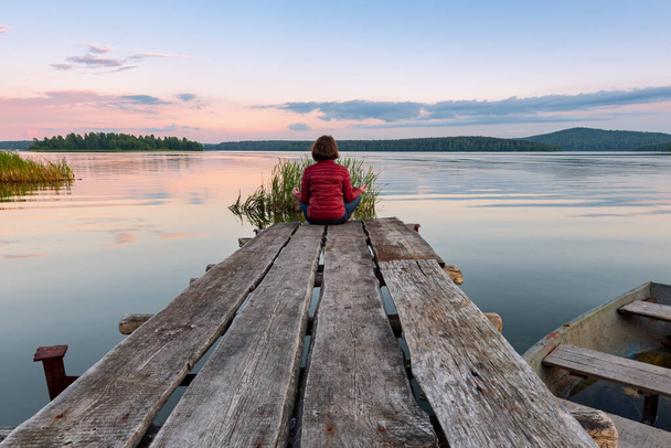 Girl sitting in lotus position on a wooden pier - Foto, afbeelding