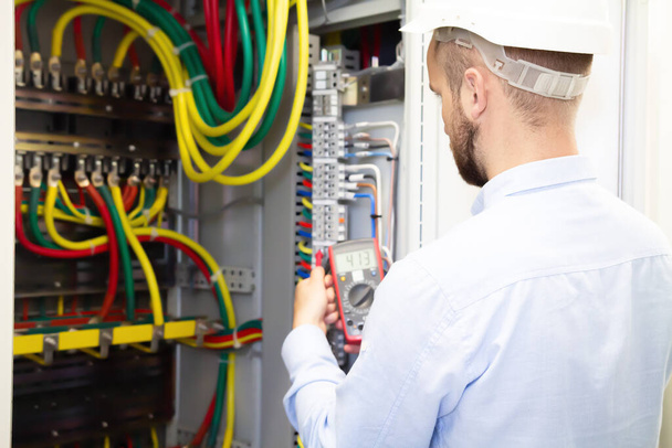 Electrician engineer measures voltage in power electrical cabinet. Serviceman adjusts fuse box. - Fotoğraf, Görsel