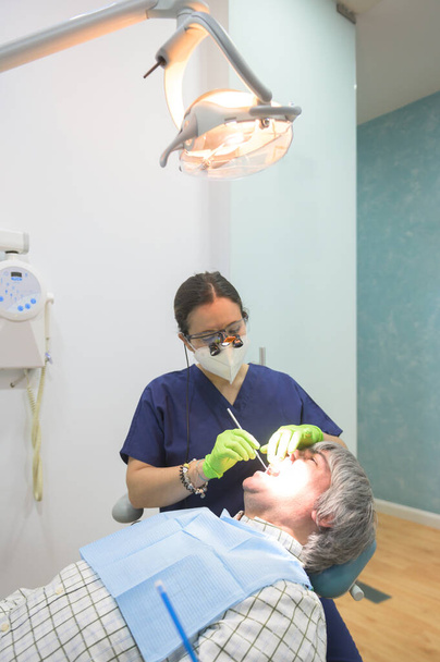 Mladá zubařka se sanitární maskou, vyšetřuje pacientku na zubní klinice. Koncept péče o zuby - Fotografie, Obrázek