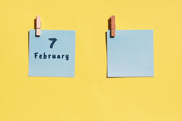 - 7 lutego. 7. dzień miesiąca, data kalendarzowa. Dwie niebieskie kartki do pisania na żółtym tle. Widok z góry, odbiór. Miesiąc zimowy, koncepcja dnia roku - Zdjęcie, obraz