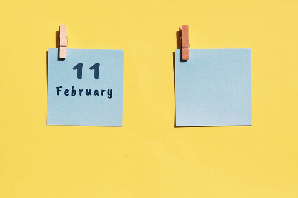 11 de febrero. Día 11 del mes, fecha del calendario. Dos hojas azules para escribir sobre un fondo amarillo. Vista superior, espacio de copia. Mes de invierno, concepto del día del año - Foto, imagen