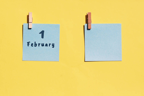 1. Februar. 1. Tag des Monats, Kalenderdatum. Zwei blaue Blätter zum Schreiben auf gelbem Hintergrund. Draufsicht, Kopierraum. Wintermonat, Tag des Jahres. - Foto, Bild