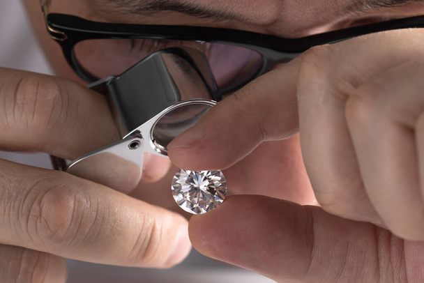 Jeweller asian man looking at diamond through magnifying glass. Diamond dealer evaluating and grading big size gem stone. - Foto, Bild