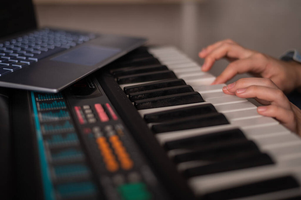 Női kezek közelsége az elektromos zongorán. Egy nő megtanul szintetizátorozni egy laptopon. - Fotó, kép