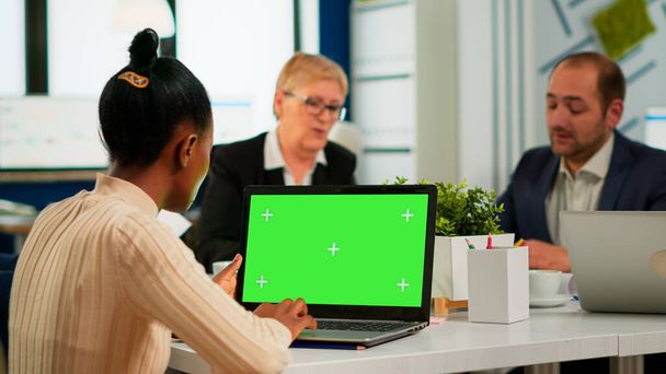 Afrikanische Managerin sitzt am Konferenztisch und blickt auf Laptop mit grünem Bildschirm - Foto, Bild