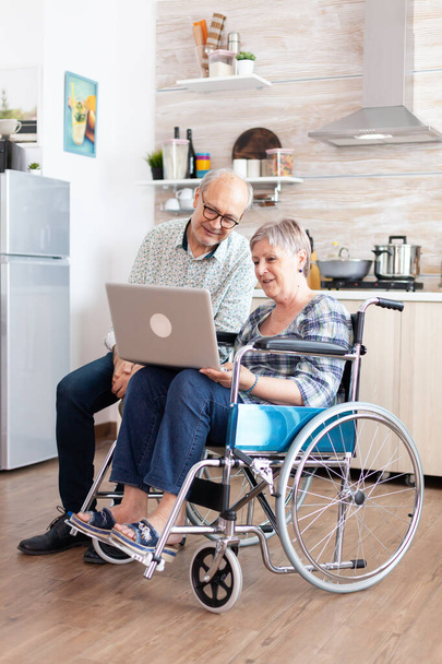 Paralyzed senior woman in wheelchair and husband browsing on internet - Fotoğraf, Görsel