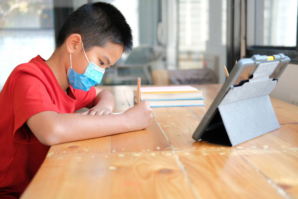 Yüz maskesi takan Asyalı çocuk internette ders çalışıyor. uzak buluşma uzaklığı eğitimi evde - Fotoğraf, Görsel