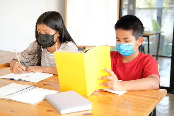 asian girl boy student wearing face mask studying writing notes doing homework in library. learning education at school - Fotoğraf, Görsel