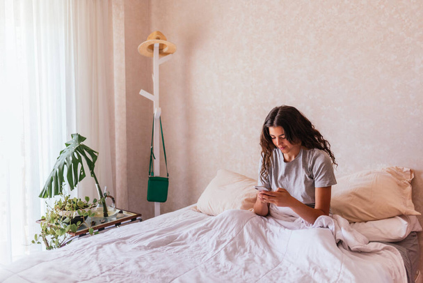 ベッドの上で彼女の携帯電話を使用してパジャマで幸せな女の子のストック写真. - 写真・画像