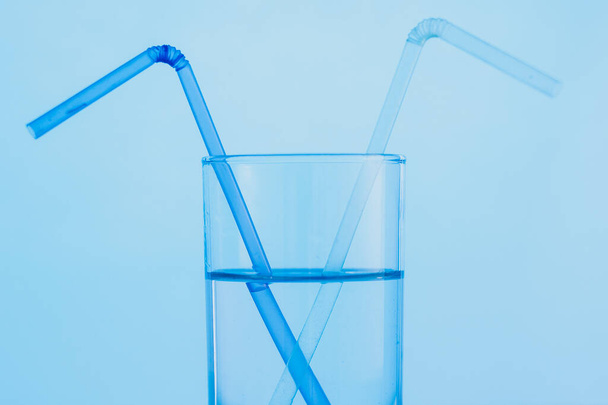 2本の飲み物用ストロー付きの澄んだ青い水のガラス。世界水の日の概念. - 写真・画像