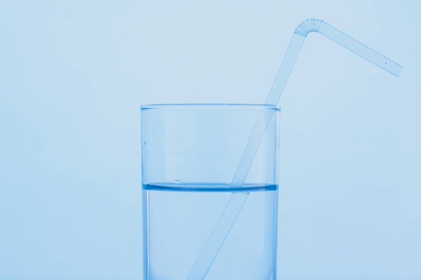 Ein Glas klares blaues Wasser mit einem Trinkhalm. Das Konzept des Weltwassertages. - Foto, Bild