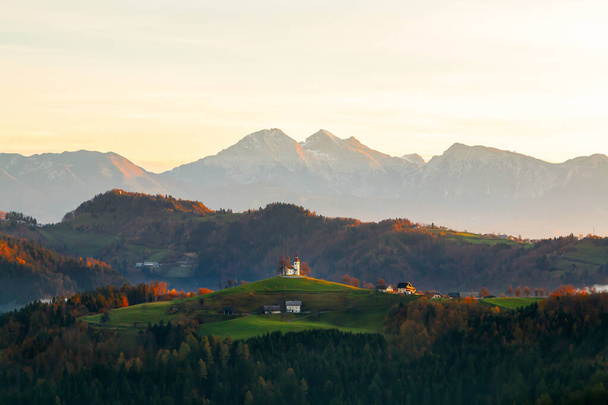Iglesia Sveti Tomaz (Santo Tomás) en una colina a la salida del sol hermosa en otoño, cerca de Skofja Loka en la región de Carniola superior en Eslovenia - Foto, imagen