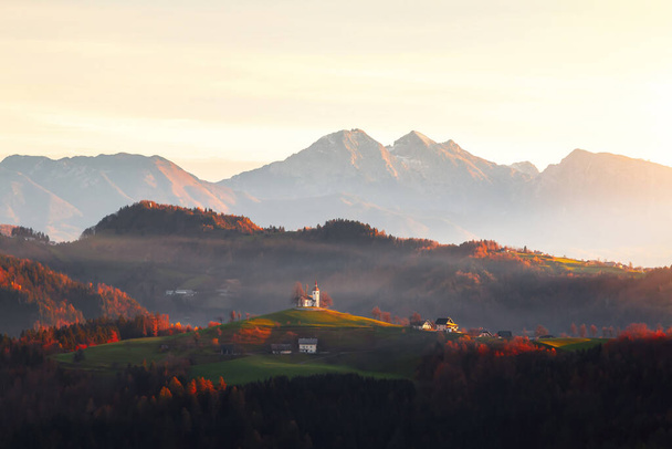 Iglesia Sveti Tomaz (Santo Tomás) en una colina a la salida del sol hermosa en otoño, cerca de Skofja Loka en la región de Carniola superior en Eslovenia - Foto, imagen