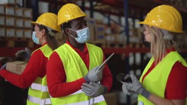 Team working together in warehouse doing inventory using digital tablet and loading delivery boxes while wearing face mask during corona virus outbreak - Logistic and industrial concept - Footage, Video
