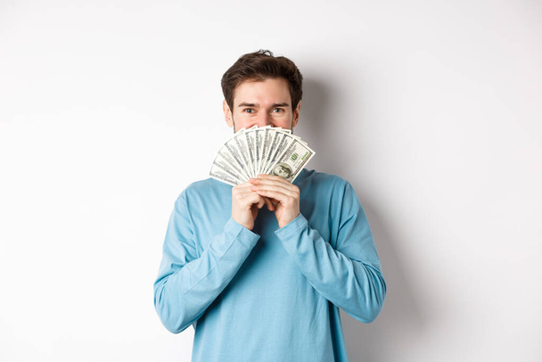 Cheerful shopper holding money for shopping, standing with dollars and smiling, standing over white background in casual clothes - Foto, afbeelding
