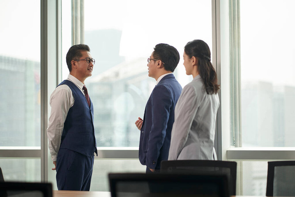 kolme aasialaista liikemiestä miehet ja naiset seisomassa puhumassa ikkunan edessä toimistossa kokoushuone - Valokuva, kuva