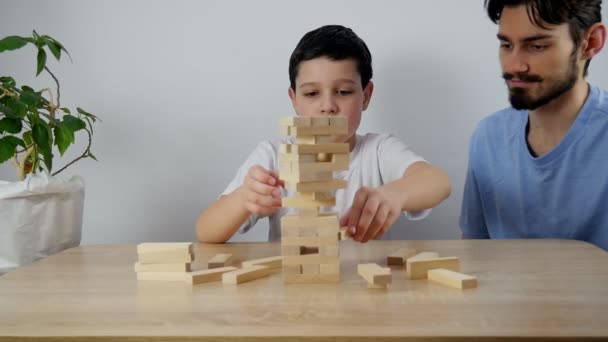 Семья из двух человек играет в настольную игру с деревянной башней дома. Два брата играют и чихуахуа. - Кадры, видео