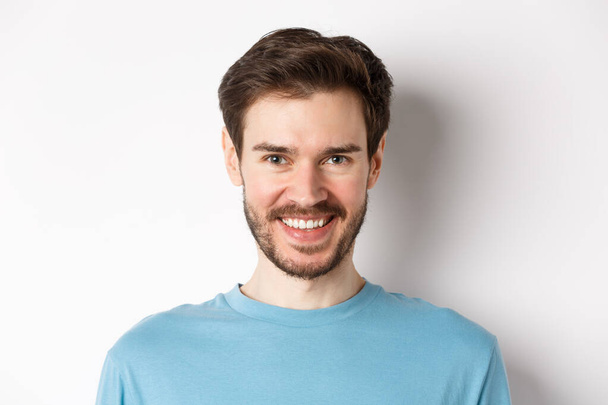 Közelkép jóképű kaukázusi férfi mosolygós fehér fogak, nézi a kamera, álló kék ing fehér háttér - Fotó, kép