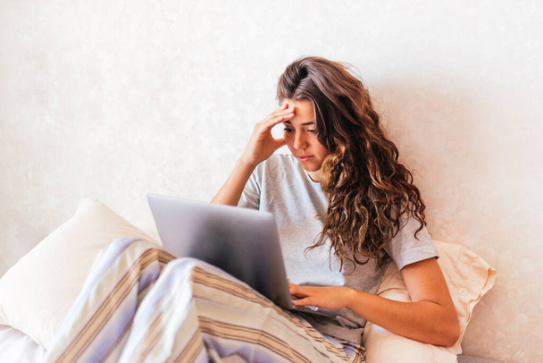 Склад фото стрессовой девушки в пижаме с помощью компьютера в постели. - Фото, изображение