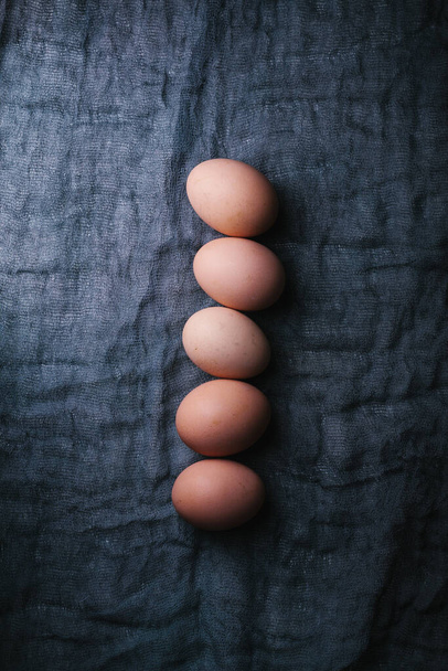 Αυγά σε σκούρο φόντο υφάσματος. Έννοια του Πάσχα, της άνοιξης ή του οικολογικού φαγητού. Πάνω όψη - Φωτογραφία, εικόνα