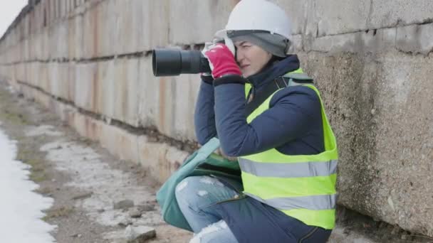 Női mérnök biztonsági sisakkal és fényképezőgéppel az építkezésen - Felvétel, videó