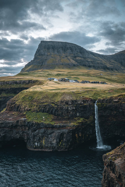 Gasadalur village and Mulafossur its iconic waterfall during sunset in summer with bluw sky. Vagar, Faroe Islands, Denmark. Rough see in the north atlantic ocean. - Foto, Bild
