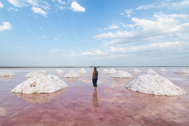 Mujer de pie en llanuras de sal marina muerta con las pirámides de sal excavada. Color agua con algas rosadas. - Foto, imagen