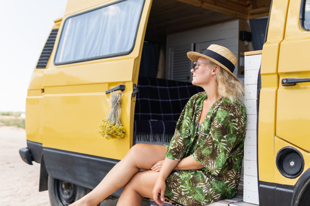 Genç sarışın kadın deniz kenarında karavanla seyahat ediyor. Otomatik inşa edilmiş karavan plaja park edilmiş.. - Fotoğraf, Görsel