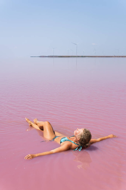 Woman swimming in dead sea salt plains. Water colored with pink algae. - Photo, Image
