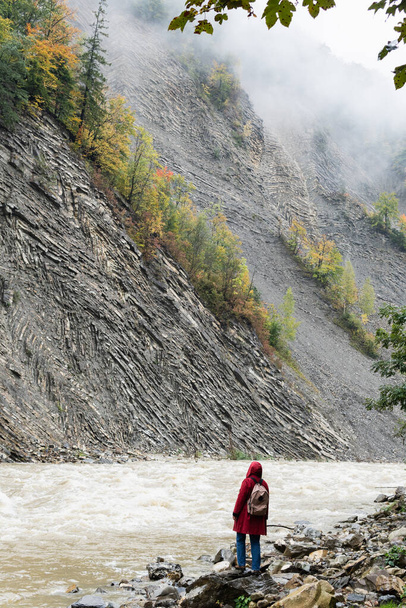 Woman in red coat standing on the banks of deep Prut river in Yaremche, Ukraine. - Photo, Image