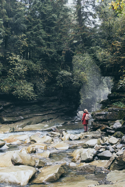 Woman in red coat standing on the banks of deep mountain river surrounded by rocky canyon walls in Yaremche, Ukraine - Photo, Image