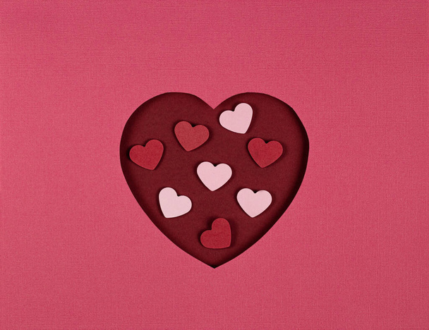 ピンクの背景に切り取られた紙の心。バレンタインデーの紙アート。紙切りやクラフトスタイル. - 写真・画像