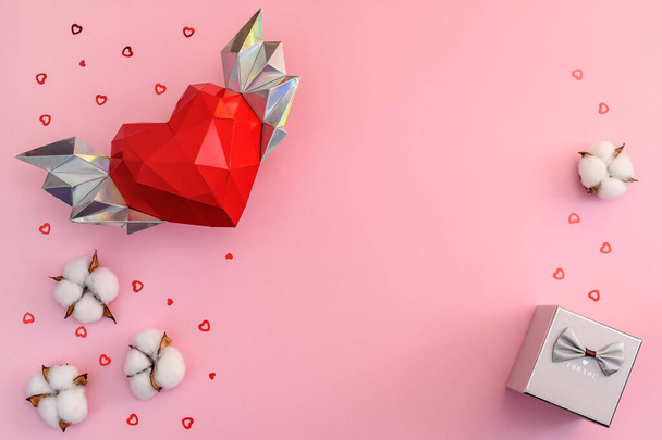 Félicitations pour la Saint-Valentin. Coeur polygonal avec ailes sur fond rose avec fleurs en coton, boîte cadeau. - Photo, image