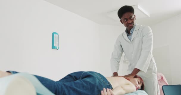 Fisioterapeuta africana realiza terapia de masaje, a la joven hembra para restaurar la fuerza muscular, en la Clínica de Rehabilitación Moderna. Salud de espalda. Kinesiología. Tratamiento de recuperación. Rehabilitación. - Metraje, vídeo