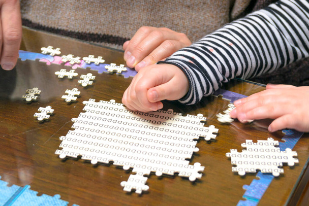Zbliżenie rąk dziewczyny i jej ojca układających puzzle przy stole w salonie. Autentyczna koncepcja hobby domowego. - Zdjęcie, obraz