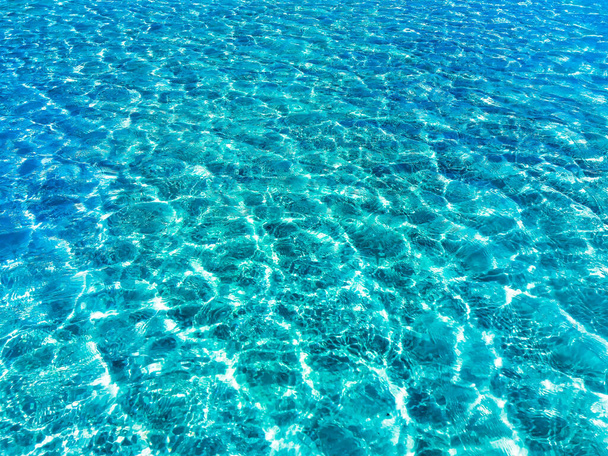 Průhledná tyrkysově modrá mořská voda na pozadí bílého písku na dně, horní pohled. Slunce svítí na povrch. Kvalitní foto - Fotografie, Obrázek