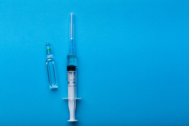 Μια σύριγγα με ένεση σε μπλε φόντο ως σύμβολο εμβολιασμού κατά την πανδημία από το coronavirus. - Φωτογραφία, εικόνα