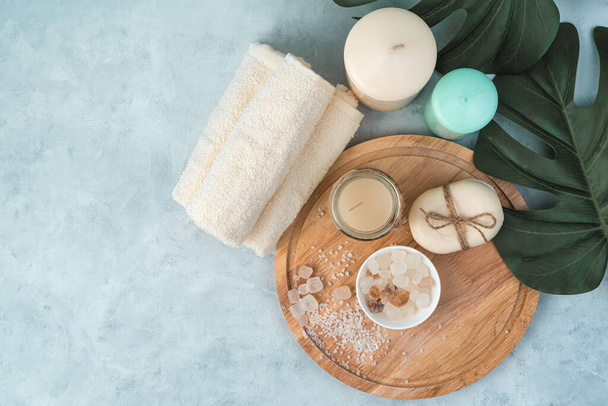 Candles, towels, soap, salt on a wooden board on a light blue background with monstera leaves. - Foto, imagen