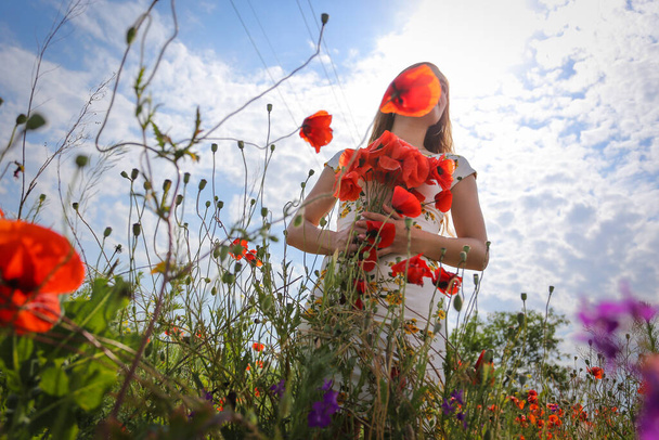 Mavi gökyüzünün arka planında bir buket gelincik taşıyan bir kızın silueti. fotoğraf çiçekler aracılığıyla çekildi - Fotoğraf, Görsel