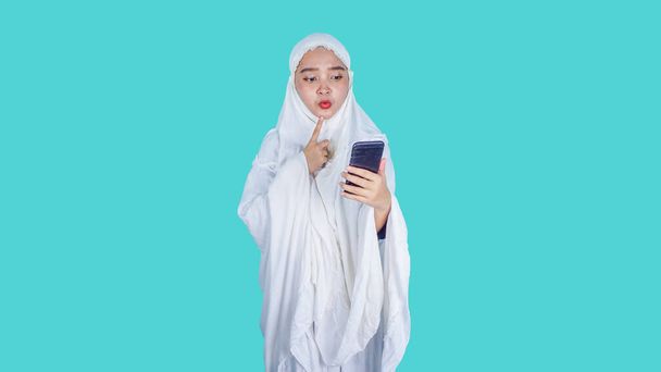 Ramadan, Ied Fitr, Ied Mubarak Concept - Serious asian woman wearing muslim hijab scarf mukena holding phone browse internet reading media.  - Photo, Image